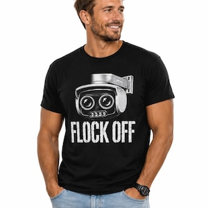 Puede incluir: Una camiseta negra de manga corta con un gráfico de una cámara de seguridad plateada con dos lentes grandes y el texto "FLOCK OFF" impreso en letras mayúsculas blancas debajo de la ilustración de la cámara en la parte frontal.