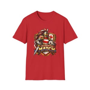 Op de afbeelding: Rood t-shirt met een afbeelding van een ridder in harnas met een zwaard en een voetbal. Het ontwerp bevat de tekst "THIS IS NOT MY FIRST MATCH" op een schild met een esdoornblad.