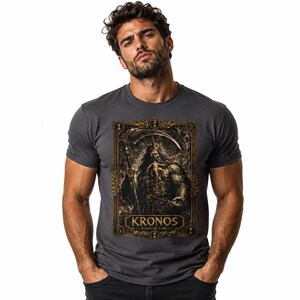 May include: A charcoal gray short-sleeve t-shirt featuring a rectangular graphic print of a bearded figure holding a scythe and a small child. The design is framed in gold with the text KRONOS TITAN OF TIME printed in a bold, serif font at the bottom.