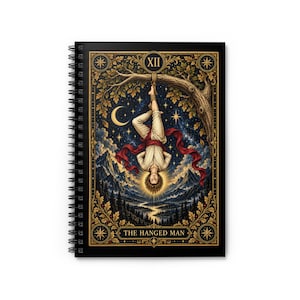 Könnte beinhalten: Ein spiralgebundenes Notizbuch mit einer Tarotkarten-Illustration des Gehängten. Das Bild zeigt eine Figur, die kopfüber an einem Ast vor einem Sternenhimmel, Bergen und einem Wald hängt, mit dem Text XII und THE HANGED MAN.