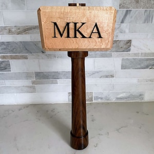 May include: A wooden gavel with a maple head and a walnut handle. The head is engraved with the letters "MKA".