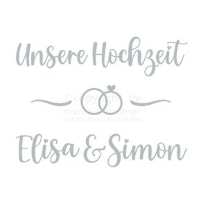Peut inclure: Un autocollant gris clair avec le texte "Unsere Hochzeit" au-dessus de deux anneaux entrelacés et les noms "Elisa & Simon". L'autocollant comprend également le texte "Aufkleber - Handschrift 20" et le nom du designer.