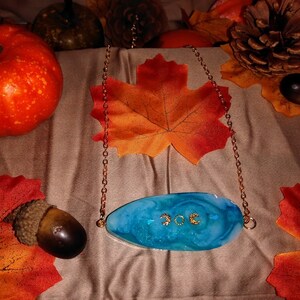 May include: A blue and white resin pendant necklace with gold glitter and a gold chain. The pendant has a swirl design and the words "JOC" in gold glitter.