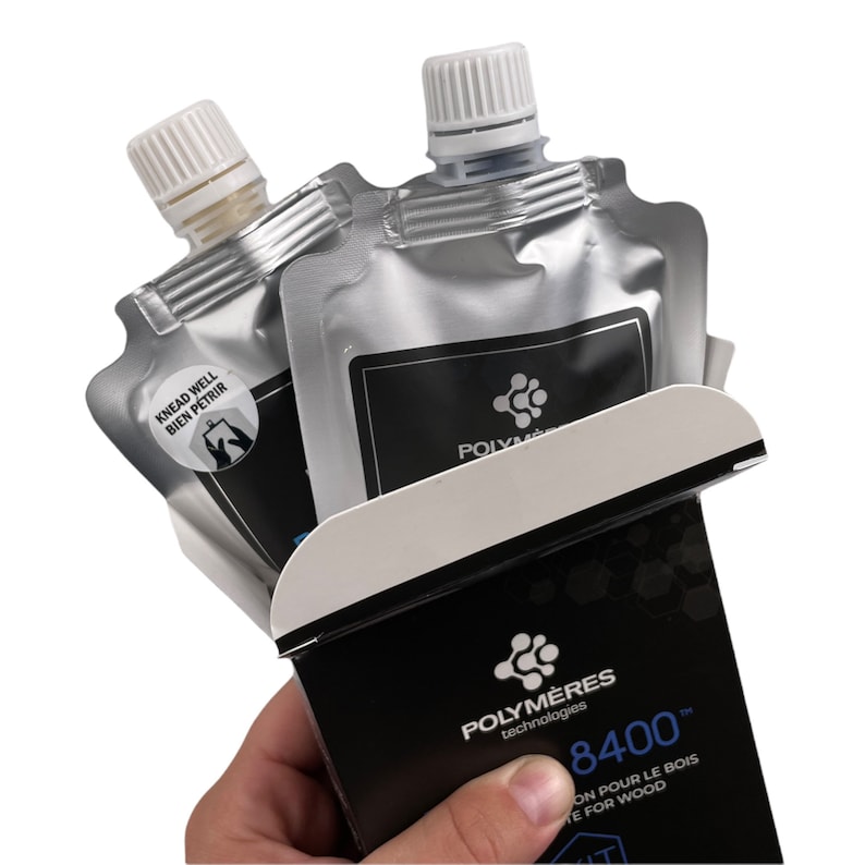 May include: Two silver pouches with white caps containing wood filler. The pouches are partially open and reveal a black box with the text "Polym&egrave;res technologies 8400&trade; On pour le bois / We for wood".