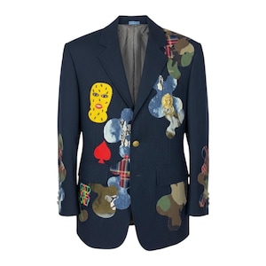 May include: A navy blue blazer featuring various colorful patches including a yellow face mask, a red spade, plaid patterns, camouflage prints, and a gold lion head door knocker ornament. The jacket has a single gold button closure and two pockets.