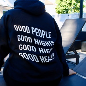 K&ouml;nnte beinhalten: Ein schwarzer Kapuzenpullover mit wei&szlig;em Text auf dem R&uuml;cken. Der Text lautet "GOOD PEOPLE, GOOD NIGHTS, GOOD VIBES, GOOD HEALTH". Dieser l&auml;ssige Pullover ist f&uuml;r den Alltag geeignet und ein bequemes Kleidungsst&uuml;ck.