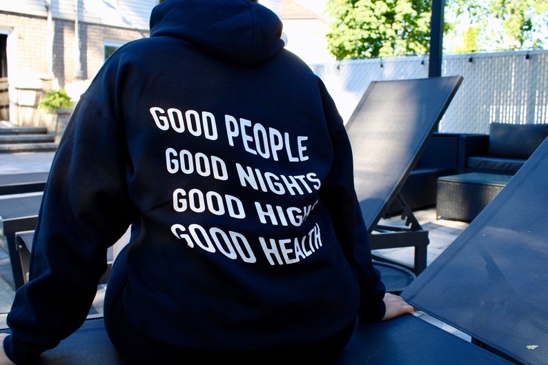 K&ouml;nnte beinhalten: Ein schwarzer Kapuzenpullover mit wei&szlig;em Text auf dem R&uuml;cken. Der Text lautet "GOOD PEOPLE, GOOD NIGHTS, GOOD VIBES, GOOD HEALTH". Dieser l&auml;ssige Pullover ist f&uuml;r den Alltag geeignet und ein bequemes Kleidungsst&uuml;ck.