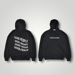 K&ouml;nnte beinhalten: Zwei schwarze Kapuzenpullover. Einer hat den wei&szlig;en Aufdruck "GOOD PEOPLE GOOD NIGHTS GOOD HIGHS GOOD HEALTH" auf dem R&uuml;cken. Der andere hat "I COUNT MY BLESSINGS" in Wei&szlig; auf der Vorderseite.