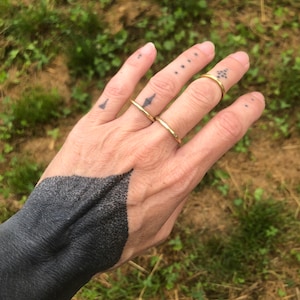 Può includere: Una mano con un tatuaggio nero sul polso e diversi anelli d'oro alle dita.