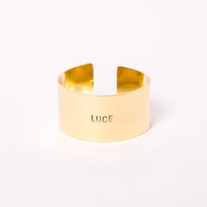 May include: A gold metal napkin ring with the word "LUCE" engraved on the front.