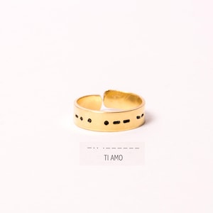 Op de afbeelding: Een gouden ring met de woorden "TI AMO" in morsecode gegraveerd op de band.