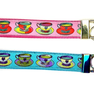 Peut inclure: Deux porte-clés avec un motif de tasse à thé. L'un est rose avec des tasses à thé rouges, jaunes et vertes. L'autre est bleu avec des tasses à thé violettes, jaunes et vertes. Chaque porte-clés a un fermoir et un anneau en métal.