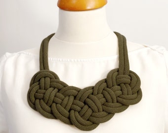 Op de afbeelding: Een groene geknoopte touwketting met een groot, ingewikkeld ontwerp. De ketting wordt getoond op een wit mannequin.