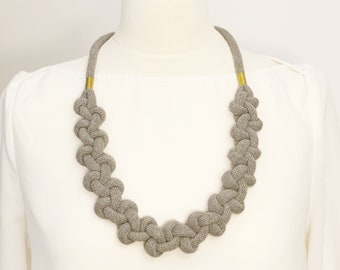 Op de afbeelding: Een grijze geknoopte ketting met gouden accenten. De ketting is gemaakt van een zachte, geweven stof en heeft een eenvoudig, elegant ontwerp.