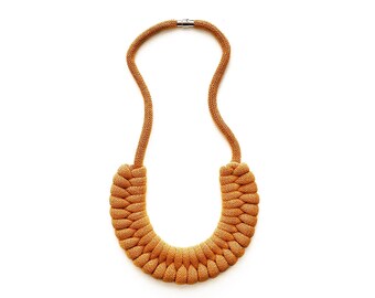 Op de afbeelding: Een mosterdgele touwketting met een gevlochten ontwerp. De ketting is gemaakt van een dik, zacht touw en heeft een eenvoudige metalen sluiting.