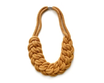 Op de afbeelding: Een mosterdgele touwketting met een gevlochten ontwerp. De ketting is gemaakt van dik touw en heeft een eenvoudige metalen sluiting.