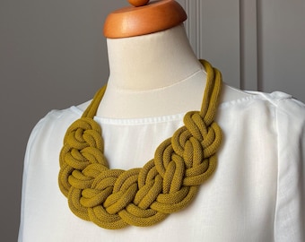 Op de afbeelding: Een geknoopte ketting van dik touw in mosterdgeel. De ketting heeft een stoer, duidelijk ontwerp.