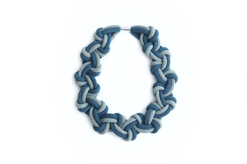 Puede incluir: Un collar azul y gris anudado hecho de cuerda de tela. El collar es un c&iacute;rculo y tiene un cierre plateado.