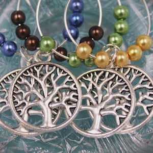 May include: Silver-toned tree of life charms with colorful beaded accents. The beads are in shades of blue, brown, green, and gold. These charms are attached to silver hoops.
