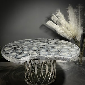 May include: A round, grey and white agate table with a silver metal base. The table top has a unique, organic shape and is made of polished agate.