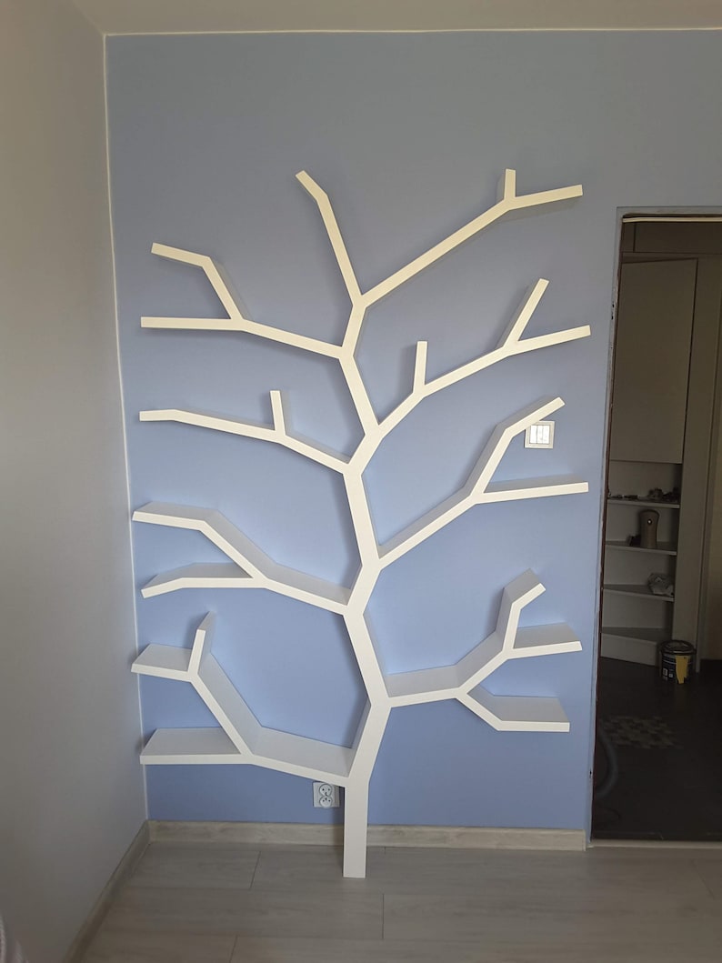 May include: White tree-shaped bookshelf with multiple shelves, mounted on a light blue wall. The bookshelf has a modern design and is perfect for displaying books, plants, or other decorative items.