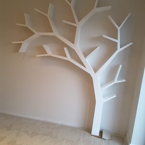 Pu&ograve; includere: Una mensola a muro bianca a forma di albero. La mensola &egrave; montata su una parete beige e ha diversi rami che fungono da ripiani. Il design &egrave; moderno e minimalista, adatto per esporre libri o oggetti decorativi.