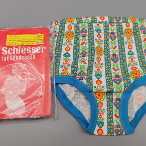 Könnte beinhalten: Vintage Unterhose mit farbenfrohem Blumenmuster und blauem Besatz. Daneben eine rote Verpackung mit der Marke "Schiesser" und dem Text "tausendsassa". Die Unterhose hat einen weißen Hintergrund mit vertikalen Streifen aus Blumen und Herzen.