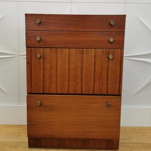 Könnte beinhalten: Ein Holzschränkchen mit vier Schubladen und einer Tür. Der Schrank hat eine hellbraune Farbe und Messingknöpfe.