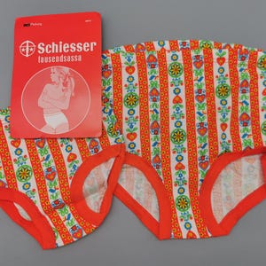 Op de afbeelding: Vintage ondergoedset met een kleurrijk bloemen- en streepjespatroon in rood, wit, groen en geel. Het ondergoed heeft een oranje rand. Een rood label met de merknaam "Schiesser" is inbegrepen.