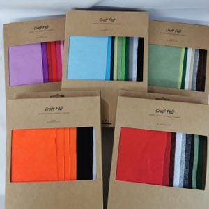 May include: A selection of craft felt sets in cardboard packaging. Each set contains a variety of felt colours, including pink, purple, blue, green, orange, red, black, white, and brown. The packaging is labelled with the words "Craft Felt".