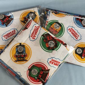 May include: Packaged fabric squares with Thomas & Friends designs. The squares have a white background with illustrations of Thomas the Tank Engine and other train characters in circular frames. The text "Thomas & Friends" is displayed in a cloud-shaped banner.