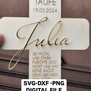 May include: A wooden cross with the name "Julia" engraved in gold lettering. The cross also features the text "Zur Taufe 19.03.2024" and a quote in German: "Sei mutig und stark! Furchte dich nicht und hab keine Angst, denn der Herr, dein Gott unternimmst."