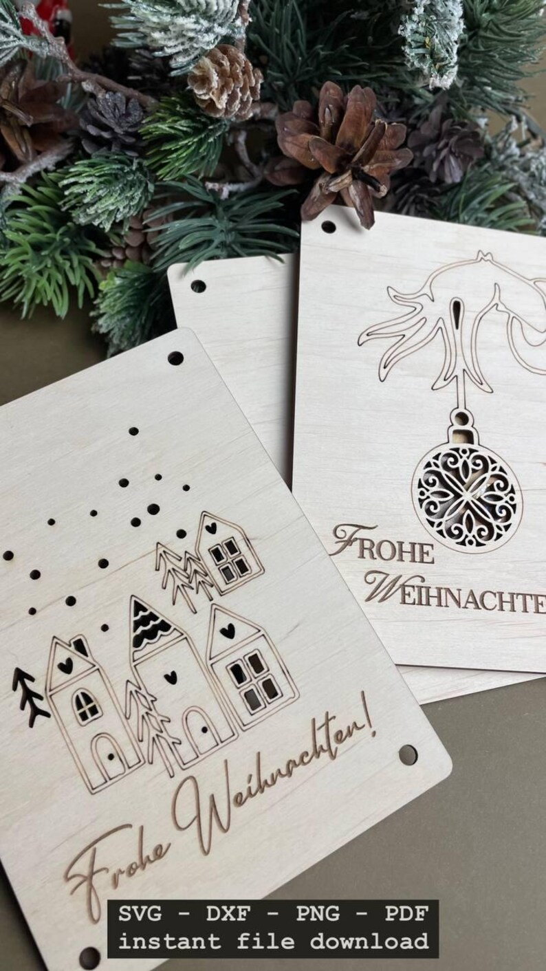 May include: Two wooden Christmas card designs. The first card features a simple design of three houses with snow falling. The second card features a Christmas tree with a hanging ornament and the text "Frohe Weihnachten!" The text at the bottom of the cards reads "SVG - DXF - PNG - PDF instant file download".