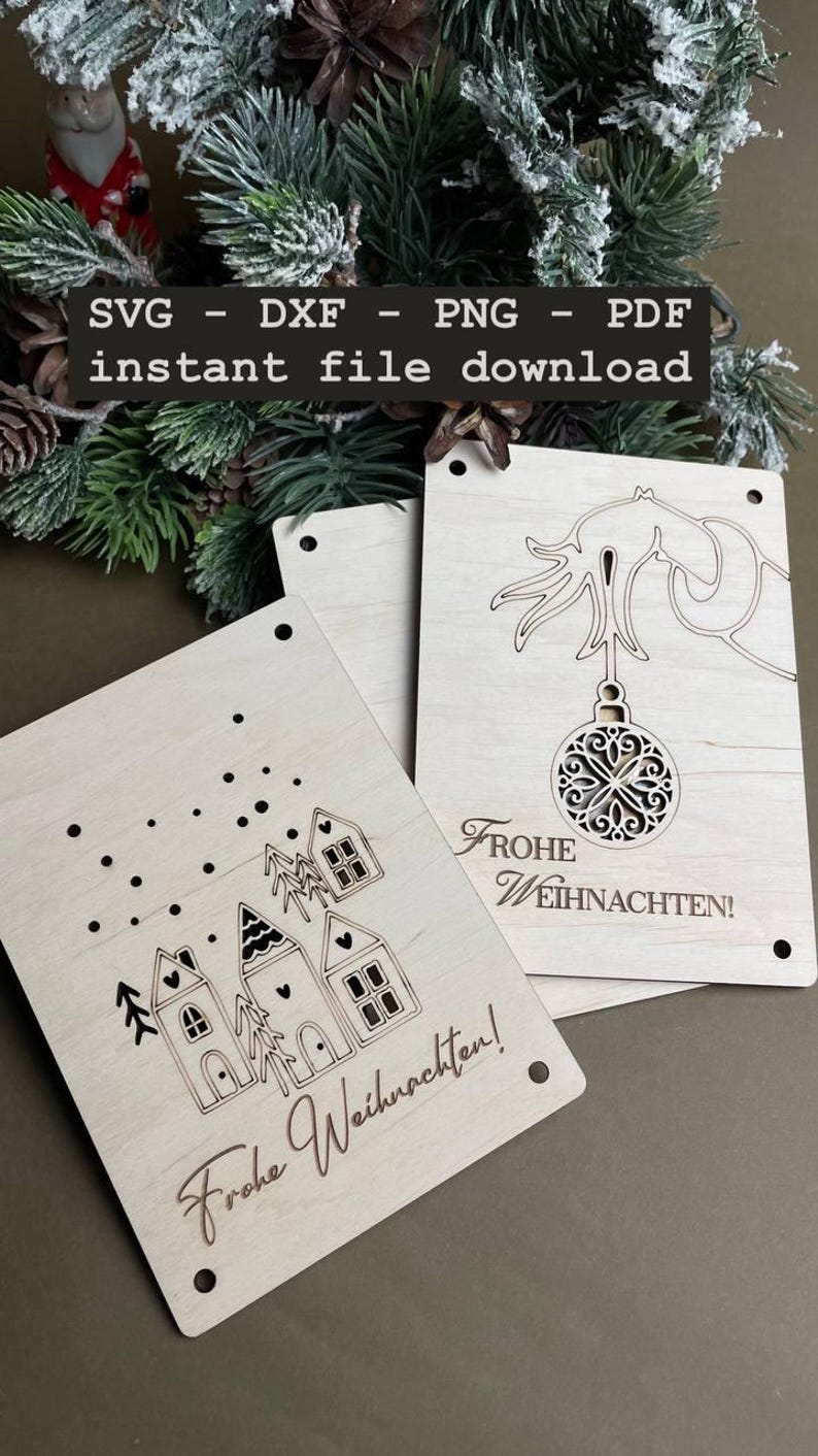 May include: Two wooden Christmas cards with laser cut designs. One card features a Christmas tree with an ornament and the text "Frohe Weihnachten!" The other card features a row of houses with the text "Frohe Weihnachten!"