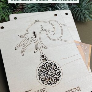 May include: A wooden Christmas ornament with a cut-out design of a Christmas tree and ornament. The ornament is light brown and has the text "Frohe Weihnachten!" on the bottom.