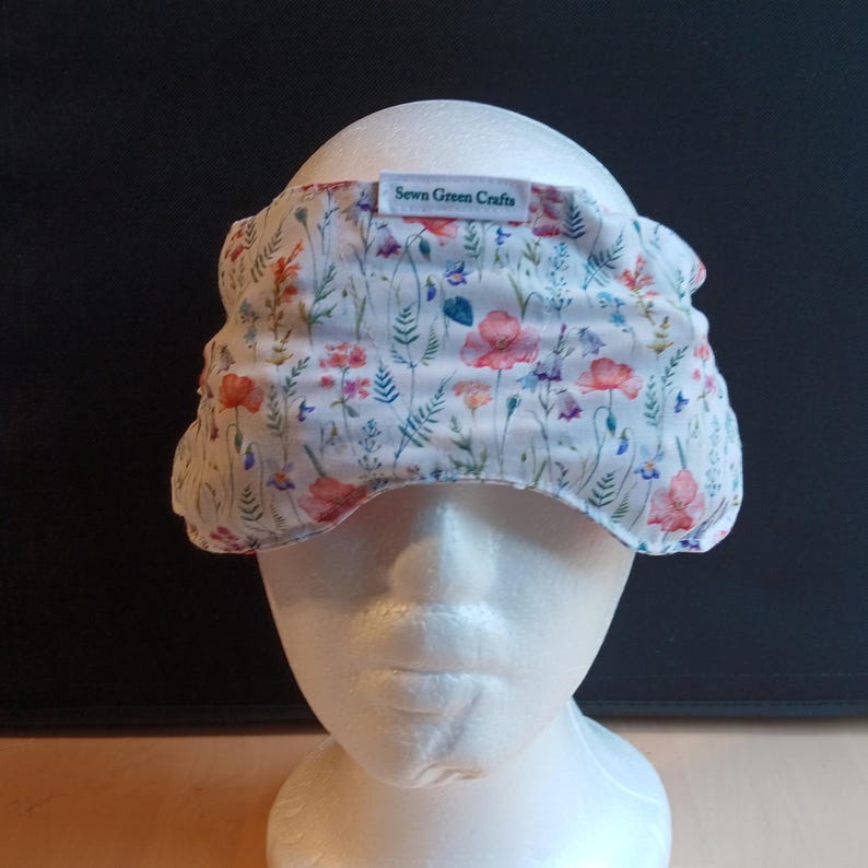 May include: A floral patterned headband featuring red, pink, and blue flowers and green leaves. The headband is displayed on a white mannequin head. The text "Sewn Green Crafts" is printed on a white label on the headband.