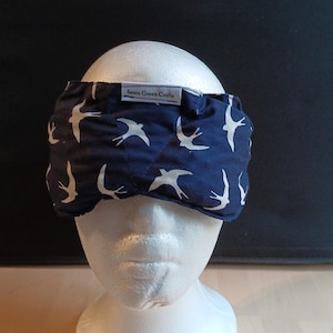 May include: A navy blue sleep mask featuring a white bird design. The mask is made of fabric and has a label that reads "Sewn Green Crafts". It is designed to block out light for improved sleep.