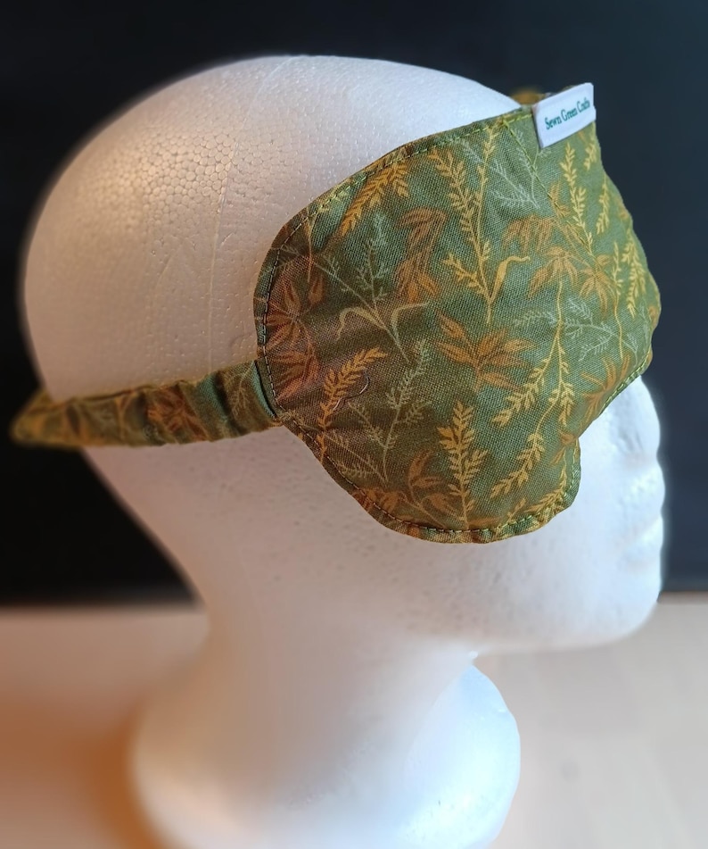 May include: A green and gold patterned sleep mask with a matching strap. The mask is made of fabric and has a label that reads "Sewn Green Crafts". The mask is designed to block out light.