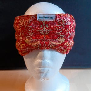May include: A red and gold patterned headband with a floral and bird design. The fabric headband features a label that reads "Sewn Green Crafts". The headband is displayed on a white mannequin head.