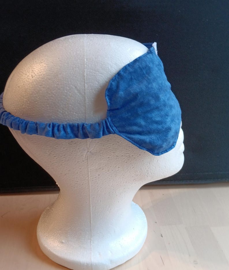 May include: A blue sleep mask with a textured pattern, designed to block out light. The mask is held in place by a blue elastic band. The sleep mask is displayed on a white mannequin head.