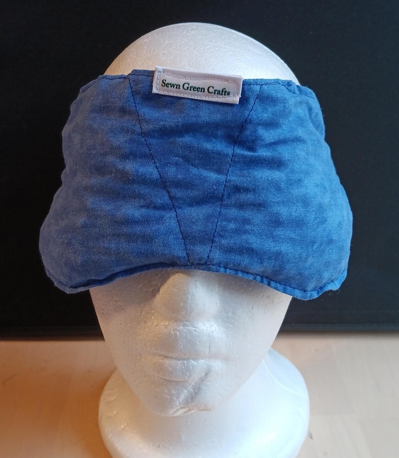 May include: A blue eye mask made from textured fabric, displayed on a white mannequin head. The mask features a label that says "Sewn Green Crafts". The mask is designed to cover the eyes and forehead.