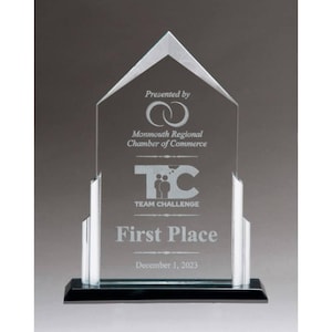 May include: A clear glass award with a black base. The award is shaped like a house with a pointed roof. It has the text "Presented by Monmouth Regional Chamber of Commerce" and "TC TEAM CHALLENGE" on it. The award also says "First Place" and "December 1, 2023".