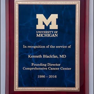 May include: A mahogany plaque with a gold border and a blue marble background. The plaque features the University of Michigan logo, the text "In recognition of the service of Kenneth Blackfan, MD", "Founding Director Comprehensive Cancer Center", and the dates "1986-2016".