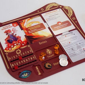 Könnte beinhalten: Ein weinroter Brettspiel-Organizer mit goldenen Akzenten, der Kartenfächer, Würfelhalter und Platz für Spielsteine bietet. Der Organizer enthält Karten mit Illustrationen und Text, und der Text "Bonus" ist sichtbar.