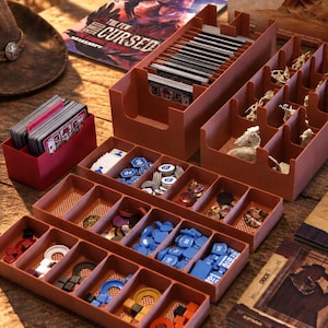 Op de afbeelding: Een set terracotta-kleurige plastic bordspelorganizers met diverse spelonderdelen, waaronder kaartspellen, kleine witte figuurtjes en diverse blauwe, rode en gele fiches, naast een kleine rode kaarthouderdoos.