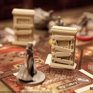 May include: A board game in play, with miniature figures and building models on a detailed game board. The game pieces are in shades of grey and beige, with a focus on the game's thematic elements.