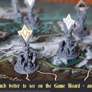 May include: Close-up of a game board with a gray, 3D printed tower with a gold and white star-shaped token on top. The board has a green and brown background with a path and the word "Fürstentu" printed on it.