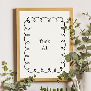 May include: A rectangular wooden frame containing a white print with a black hand-drawn curly border and the text "fuck AI" centred in a typewriter-style font. The print is displayed in a vertical orientation with a clean, minimalist aesthetic.