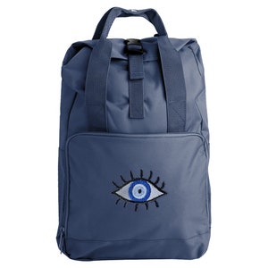 Könnte beinhalten: Ein blauer Canvas-Rucksack mit einem großen gestickten bösen Auge in Weiß, Blau und Schwarz.