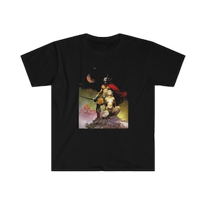 May include: A black t-shirt with a colorful illustration of a muscular figure holding a sword and a woman standing on a rocky outcrop. The background is a dark, cloudy sky with a red planet in the distance.